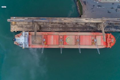 Vista aérea de um navio de carga atracado no porto de São Francisco do Sul, com estruturas portuárias e movimentação marítima ao redor.