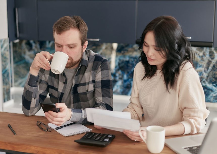 Casal analisa contas domésticas com calculadora e celular em uma cozinha.