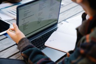Mãos usando um laptop e fazendo anotações em uma mesa de madeira