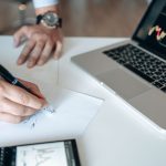 Mãos analisam dados financeiros em uma mesa com laptop e calculadora.