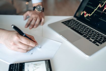 Mãos analisam dados financeiros em uma mesa com laptop e calculadora.